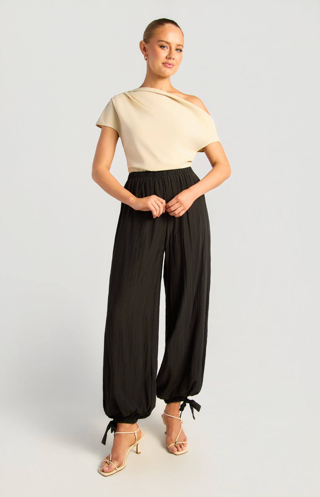 Model wearing textured balloon hem pants in black with a cream off-shoulder top
